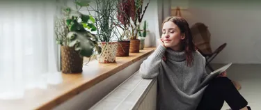 Eine Frau sitzt am Fenster vor der Heizung