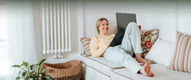 Frau liegt auf dem Sofa und schaut in ihren Notebook