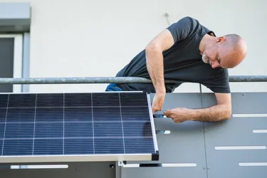 Ein Mann montiert ein Balkonkraftwerk an einem Balkongeländer
