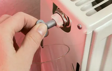 Nahaufnahme einer Hand beim Entlüften eines Heizkörpers mit einem Entlüftungsschlüssel