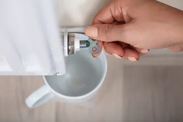 Nahaufnahme einer Frauenhand die mit einem Entlüftungsschlüssel einen Heizkörper entlüftet