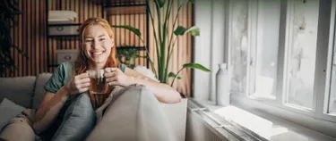 Eine Frau sitzt mit einem Tee auf dem Sofa