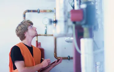 Ein junger Mann liest am Druckmessgerät einer Heizungsanlage den Druck im Kessel ab