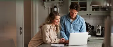 Ein Paar steht am Küchentresen und schaut auf einen Laptop