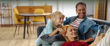 Eine Familie sitzt auf dem Sofa und schaut gemeinsam ein Smartphone.