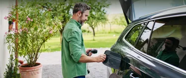 Das Bild zeigt einen Mann, der sein Elektrofahrzeug an den Strom schließt