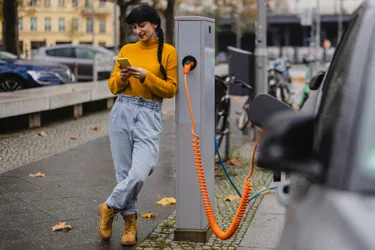 Eine junge Frau lädt ihr Elektroauto an einer öffentlichen Ladesäule