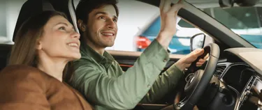 Das Bild zeigt eine Frau und einen Mann im Auto sitzend. 