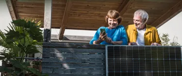 Ehepaar steht mit dem Handy auf dem Balkon vor dem Balkonkraftwerk