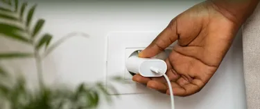 Eine Hand hält den Adapter eines in einer Steckdose steckenden Ladekabels.