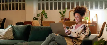 Eine Frau sitzt mit ihrem Laptop auf dem Sofa.