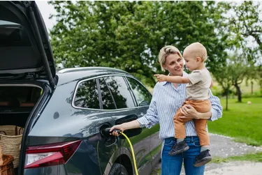 Eine Frau steht mit einem Kind auf dem Arm an einem Elektroauto