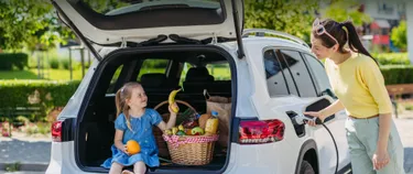 Ein Kind sitzt mit einem Obstkorb im Kofferraum eines Autos