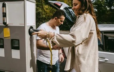 Ein Frau und ein Mann stehen an einer Ladesäule und laden ihr E-Auto auf