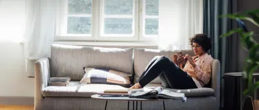 Eine Frau sitzt auf dem Sofa und schaut auf ihr Handy