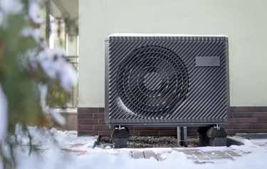 Nahaufnahme einer verschneiten vor einer Hauswand installierten Wärmepumpe