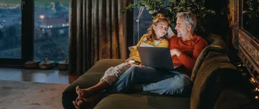 Ein Vater und seine Tochter liegen auf dem Sofa. Der Mann hat einen Laptop auf dem Schoß.