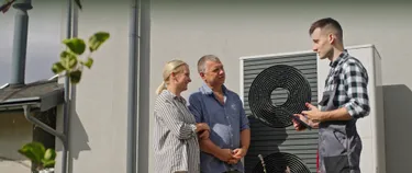 Ein Ehepaar steht neben einem Monteur vor einer Wärmepumpe