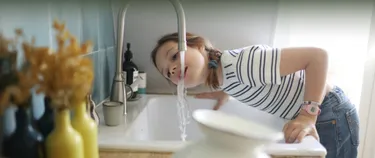 Ein Kind trinkt Leitungswasser aus dem Wasserhahn