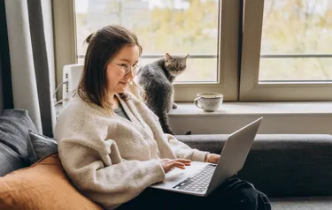 Eine Frau sitz auf einem Sofa und tippt auf einem Laptop