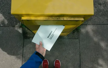 Nahaufnahme eines Briefkastens in den jemand einen Wahlbrief wirft