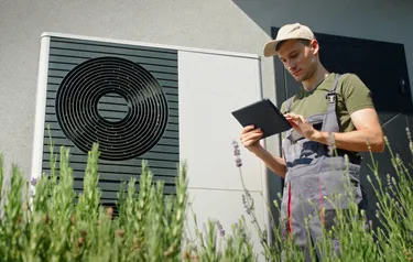 Nahaufnahme einer Wärmepumpe neben der ein Monteur steht