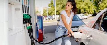 Eine Frau tankt ihr Auto an einer Tankstelle hält den Zapfhahn am Fahrzeug fest.