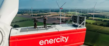 Zwei Techniker:innen stehen auf einer Windenergieanlage.