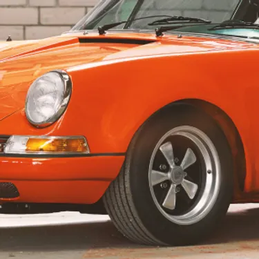 Dieses Bild zeigt einen kleinen Ausschnitt von dem vorderen Bereich eines alten, orangefarbigen Autos.