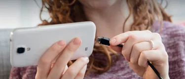 Das Bild zeigt eine Frau, die Ihr Handy an ein Ladegerät anschließt.