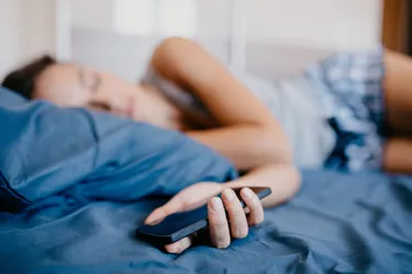 Seinen Handy-Akku sollte man nicht über Nacht laden. Das Bild zeigt ein Handy, das nachtsüber am Bett geladen wird.