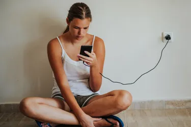 Eine Frau lädt ihr Handy an einer Steckdose.