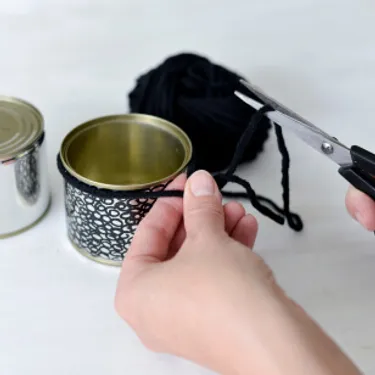 Schritt 2: Das Bild zeigt, wie die Dosen mit Wollschnüren ausgestattet werden.