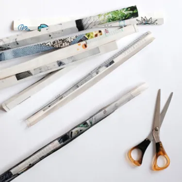 Das Bild zeigt eine Schere und mehrere zusammengefaltete Streifen aus Zeitschriftenpapier.