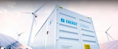 Ein Batteriespeicher sowie Solarpanels und Windräder im Hintergrund.