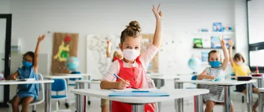 Hygienekonzept. Dieses Bild zeigt ein Mädchen in der Schule, welches eine medizinische Maske auf hat und sich gerade meldet.