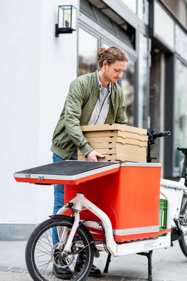 Mann belädt E-Lastenrad mit Pizza-Kartons