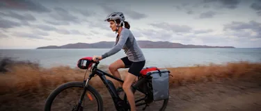 Unterschiede zwischen E-Bike, Pedelec und S-Pedelec: Das Bild zeigt eine Frau, die mit ihrem E-Bike entlang einer Küste fährt.