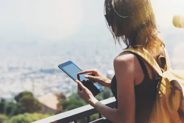 Hitze setzt Displays und Akkus stark zu und kann zum Akkubrand führen. Das Bild zeigt eine Frau, die ein Tablet in der Sonne bedient.