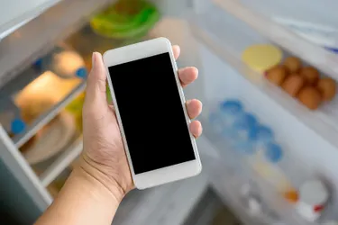 Handys zum Abkühlen in den Kühlschrank zu legen ist ein absolutes No-Go. Das Bild zeigt ein Handy, das gerade in den Kühlschrank gelegt wird.