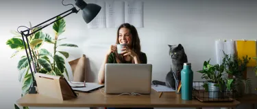Strom im Home Office sparen: das Bild zeigt eine junge Frau, die am Schreibtisch ihres Home Office sitzt und eine Tasse Kaffee trinkt.