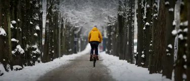 E-Bike und Pedelec im Winter fahren: Tipps für Akku, Fahrverhalten, Licht und Zubehör. Das Bild zeigt eine Frau, die bei Schnee Fahrrad fährt.