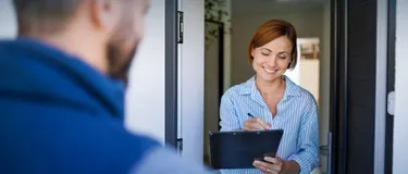 Gasumstellung: Das Bild zeigt eine junge lächelnde Frau, die einen Vertrag an der Haustür unterschreibt.