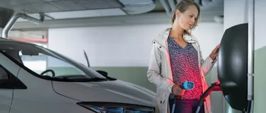 Erneuerbare Energien: Das Bild zeigt eine junge Frau an einer E-Ladesäule in einem Parkhaus.