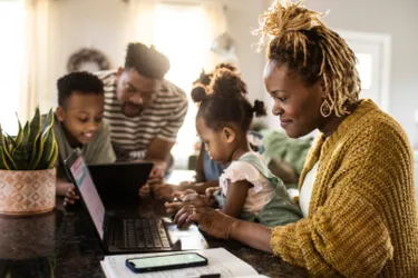 Mehrere Mitglieder einer Familie beugen sich nebeneinander sitzend über ihre Tablets, Handys und Laptops.