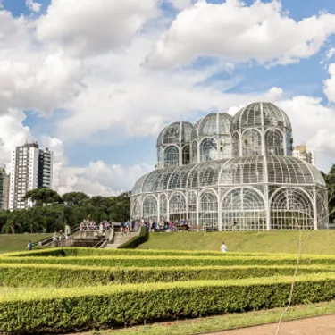 Die grünsten Städte der Welt: Curitiba, Brasilien. Das Bild zeigt ein gläsernes Gebäude in einer Parkanlage bei schönem Wetter.