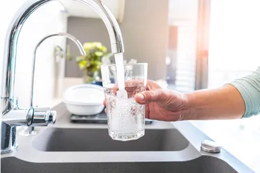 Eine Glasflasche wird am Küchenwasserhahn mit Leitungswasser aufgefüllt