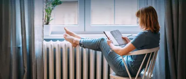 Energiesparend heizen: 5 Heizsysteme im Check. Das Bild zeigt eine junge Frau, die in ihrer beheizten Wohnung sitzt und entspannt liest.