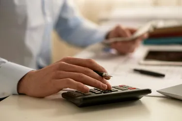 Nahaufnahme einer Männerhand, die auf einem Taschenrechner Zahlen eintippt