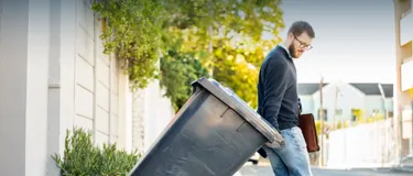 Strom aus Müll: Thermische Abfallverwertung erklärt. Das Bild zeigt einen Mann, der gerade eine graue Mülltonne an die Straße stellt.